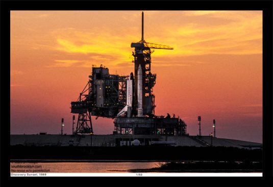 13 x 19 Framed Print, ©Mark D Phillips; the Space Shuttle Discovery on Pad 39 at Kennedy Space Center the night before its launch with a blazing sunset.
